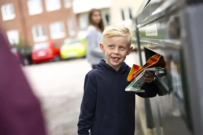 Ett barn ler mot kameran och håller olika förpackningar i handen.