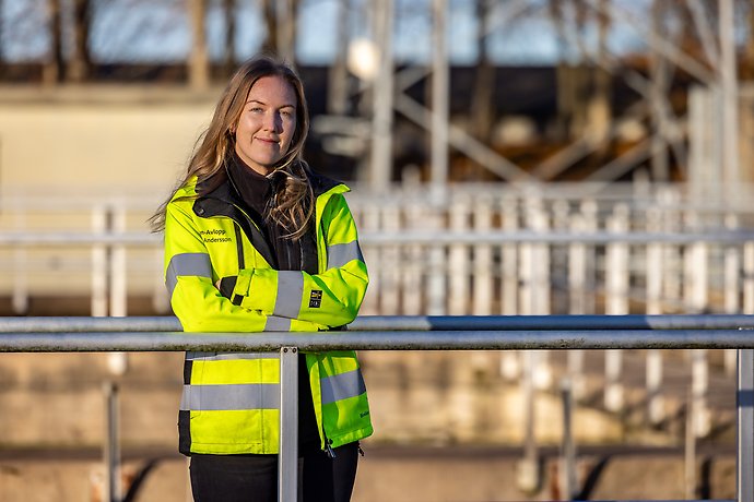 En kvinnlig arbetare inom Vatten och Avlopp som lutar sig mot ett staket